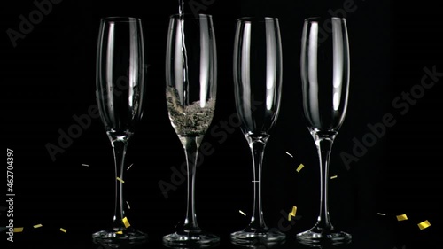 Animation of gold confetti falling over chmpagne glasses on black background photo