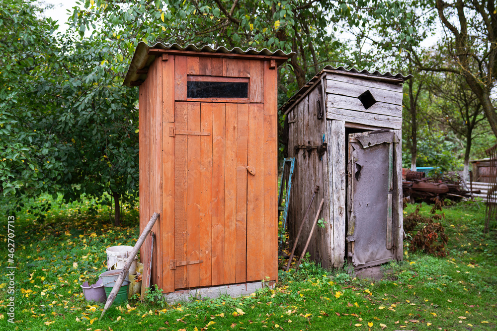Old and next to it a renovated wooden toilet in the garden outside in the open air. Old and next to it a renovated wooden toilet in the garden outside in the open air.