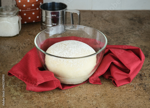 bread sourdough in a glass pan, yeast dough in a transparent bowl, wrapped in a burgundy cloth. The process of cooking homemade cakes. Beige background. Kitchen utensils in the background.