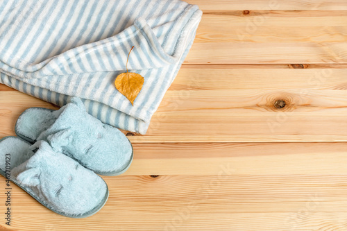 Yellow autumn leaf over striped fuzzy blanket and funny cat face blue slippers over natural wood surface. Warm fleece bedding and home shoes for cold winter season. Copy space. photo
