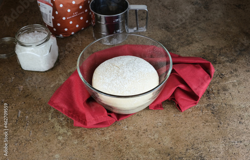bread sourdough in a glass pan, yeast dough in a transparent bowl, wrapped in a burgundy cloth. top view. The process of cooking homemade cakes. Beige background. Kitchen utensils in the background.