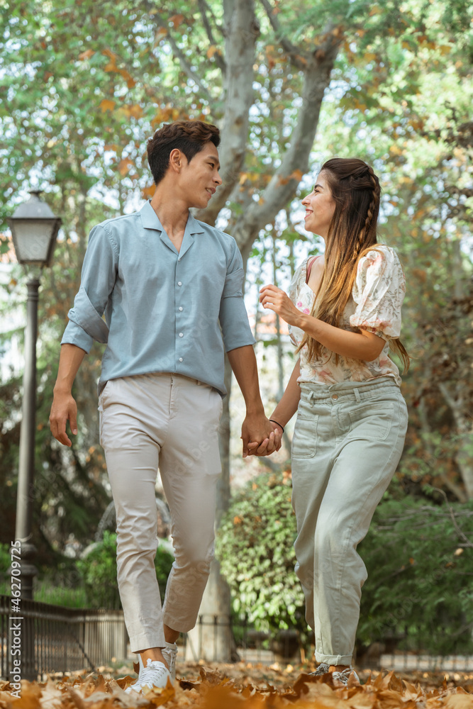 Fun interracial couple running at the park holding hands in autumn, spanish woman and korean man