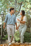 Fun interracial couple running at the park holding hands in autumn, spanish woman and korean man