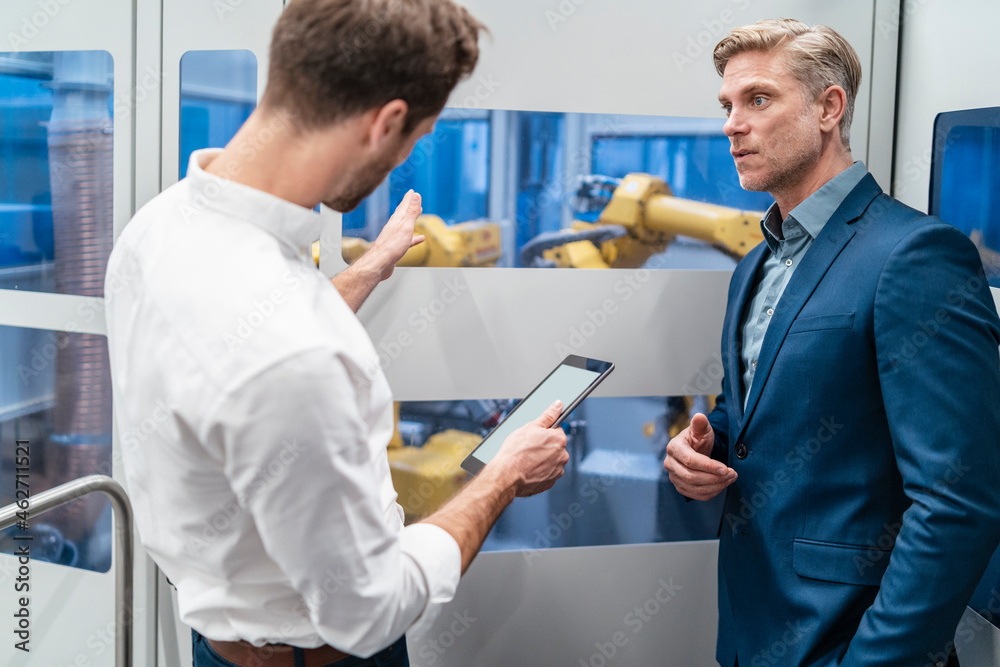 Two businessmen talking at robot in a modern factory Two businessmen talking at robot in a modern factory
