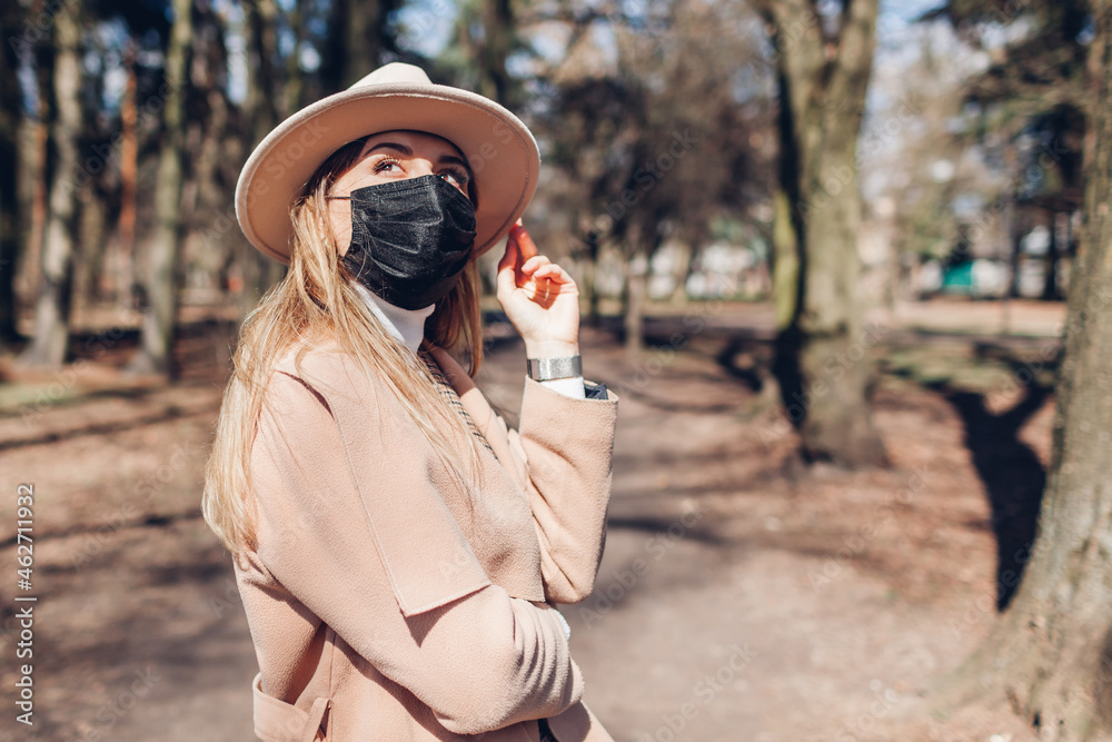 Stylish woman wears reusable mask outdoors during coronavirus covid-19 pandemic in empty spring park.