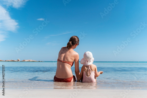 Rear view of mother with daughter sitting in the sea