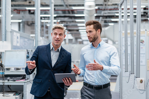 Two businessmen with tablet talking in a modern factory