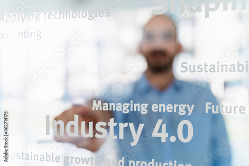 Businessman in front of glass pane pointing on words, industry 4.0