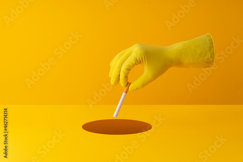 Hand dicarding cigarette into a hole in yellow background