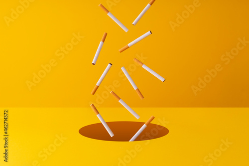 Cigarettes falling into a hole in yellow background