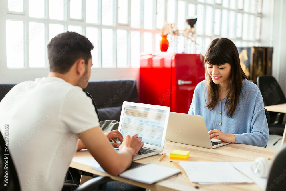 Colleagues using laptops at desk in office