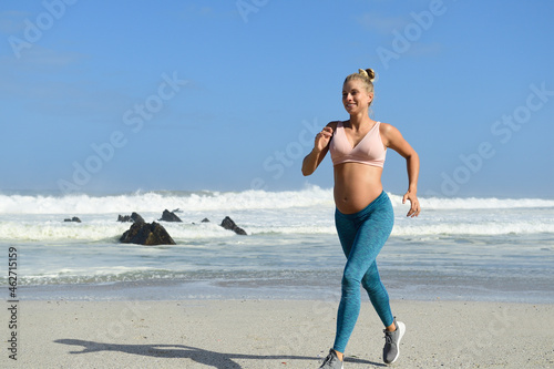 Smiling pregnant woman jogging on the beach