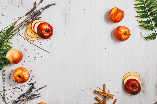 Sliced and whole apples, fern leaves, cinnamon sticks and lavender on white wood