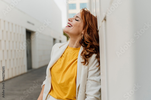 Beautiful businesswoman in white pant suit, leaning on wall, laughing