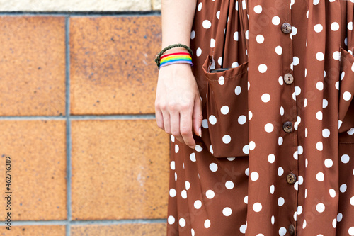 Young woman wearing brown dress with white polka dots and wristband with prismatic colours, partial view photo