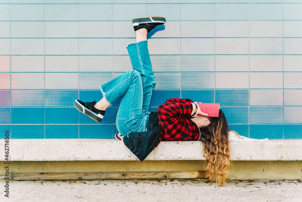 Teenage girl lying on a wall outdoors covering face with book Stock ...