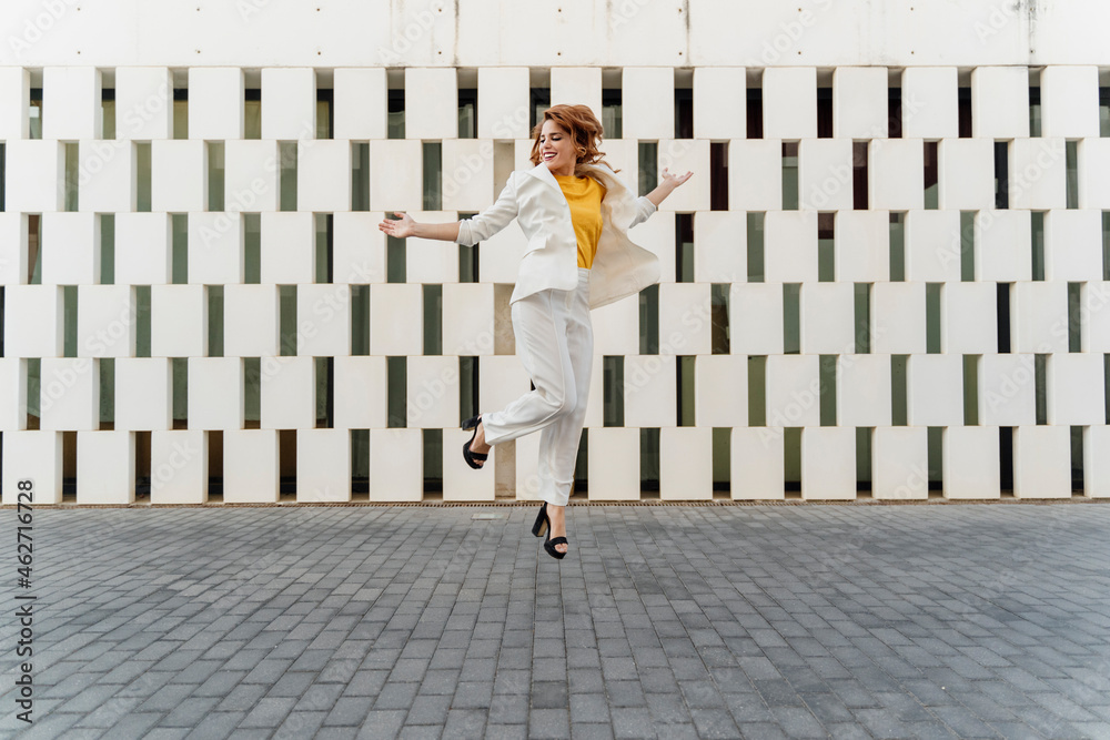 Happy businesswoman in white pant suit, jumping and dancing in the street Happy businesswoman in white pant suit, jumping and dancing in the street