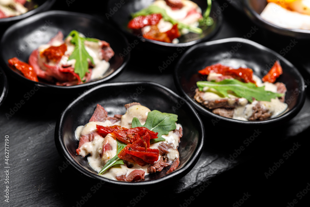 A light snack of potatoes, cucumbers, chili peppers, meat and herbs in serving cups on a dark background.