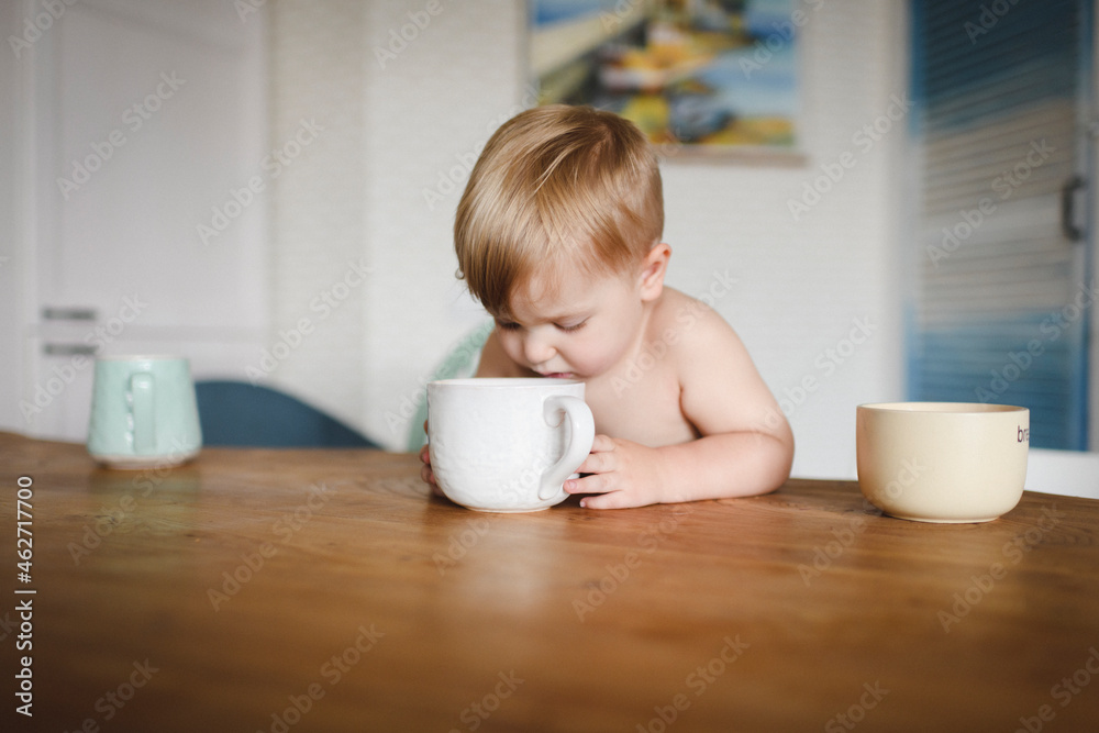 Shirtless little boy sitting at kitchen table looking into cup Shirtless little boy sitting at kitchen table looking into cup