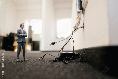 Businessman figurine standing in office, looking at disconnected cables