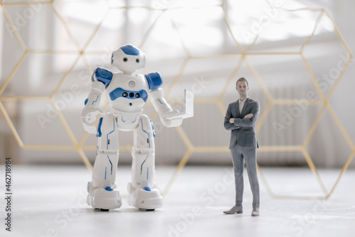 Miniature businessman figurine standing next to robot with laptop photo