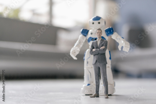 Miniature businessman figurine standing in front of robot photo