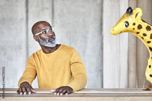 Surprised mature businessman sitting at desk in office looking at giraffe figurine photo