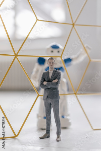 Miniature businessman figurine standing in front of robot seperated by structure photo