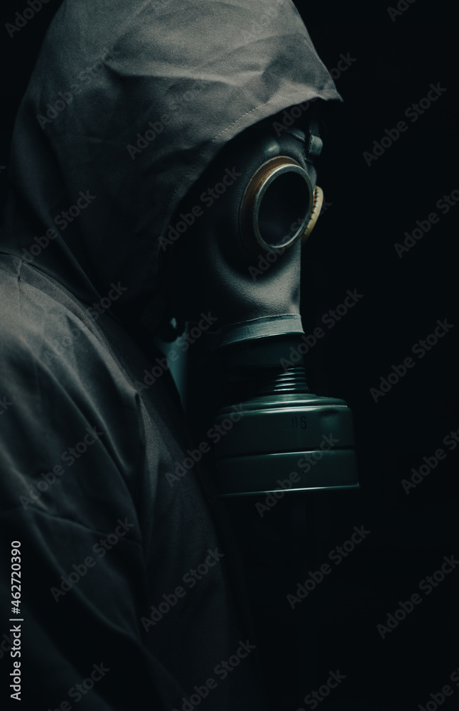 A scary man in a cloak wearing a gas mask. Dark background. Side view.