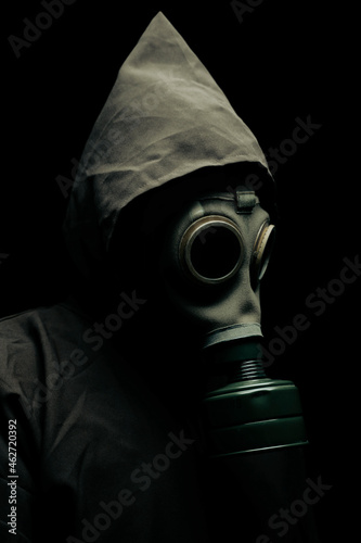 A scary man in a cloak wearing a gas mask. Dark background. Side view.