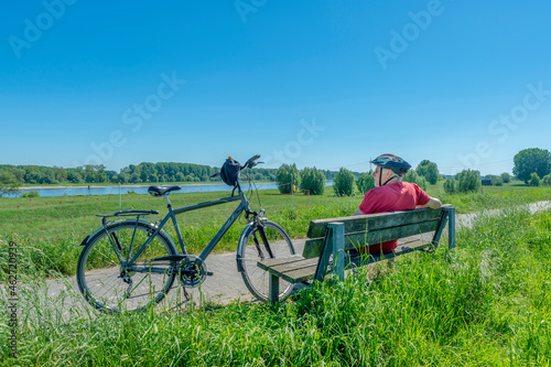 Germany, Zons, senior man with bicycle resting on a bench looking at view