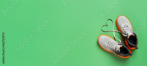 Heart shape shoe lace symbol gray textile sneakers over grassy green background. Active lifestyle, fitness and sport wide banner mockup with copy space. Shoelace heart of stylish sport shoes.