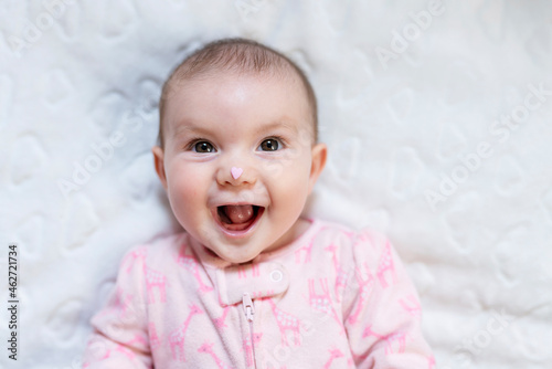 Portrait of happy baby girl with pink heart-shaped candy on nose photo