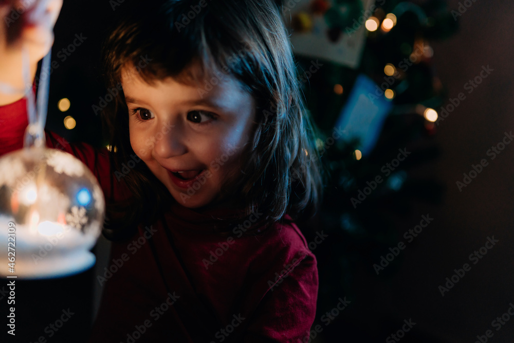 Portrait of excited little girl holding lighted glass ball at Christmas time