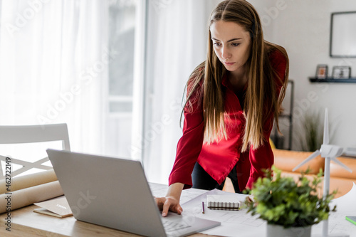 Woman in office working on plan and laptop with wind turbine model on table photo