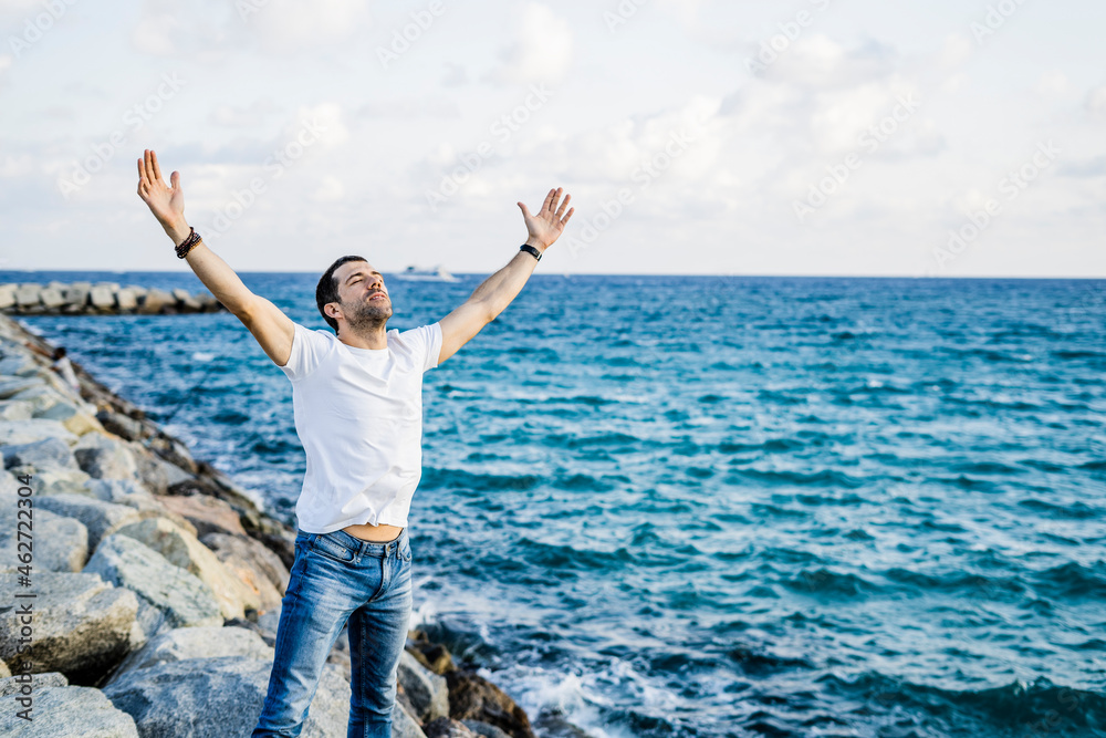 Man with raised arms and eyes closed standing in front of the sea Man with raised arms and eyes closed standing in front of the sea