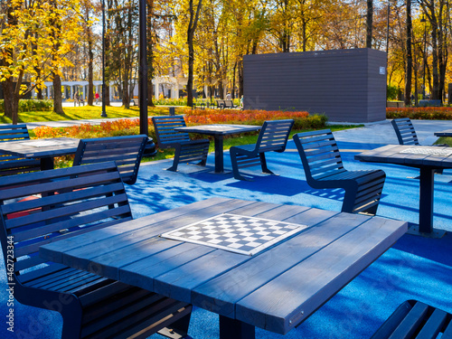 Empty tables with chessboards in the autumn park. Blue chess tables against the background of yellow trees in the city park on a sunny day. Board games in the city park in the open air.