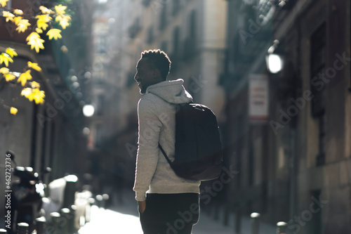 Young man with backpack looking away while standing on street in city photo
