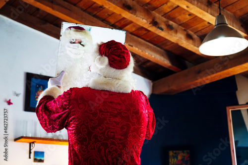 Man wearing Santa Claus costume looking in mirror while standing at home photo