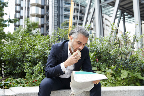 Entrepreneur reading newspaper while eating food in city photo