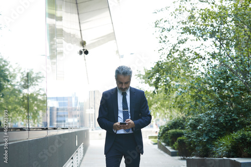 Businessman texting through smart phone while standing outside office in city
