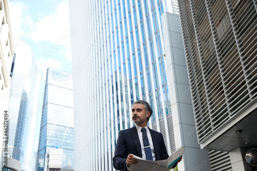 Entrepreneur with newspaper looking away outside office building in city Entrepreneur with newspaper looking away outside office building in city