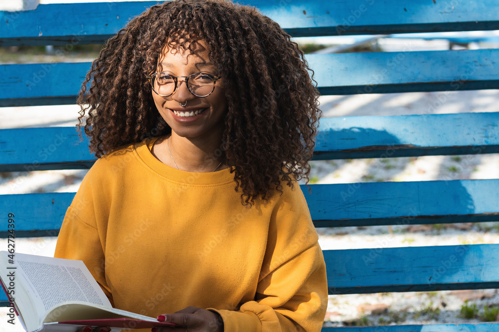 Happy young woman holding book while sitting on blue bleachers
