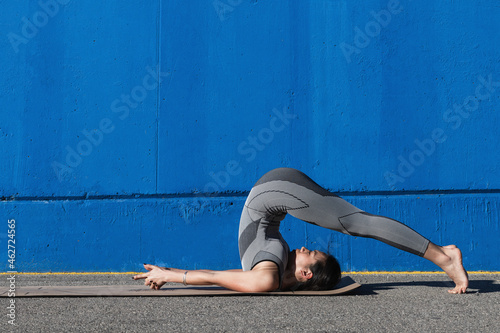 Flexible woman doing Halasana by blue wall photo