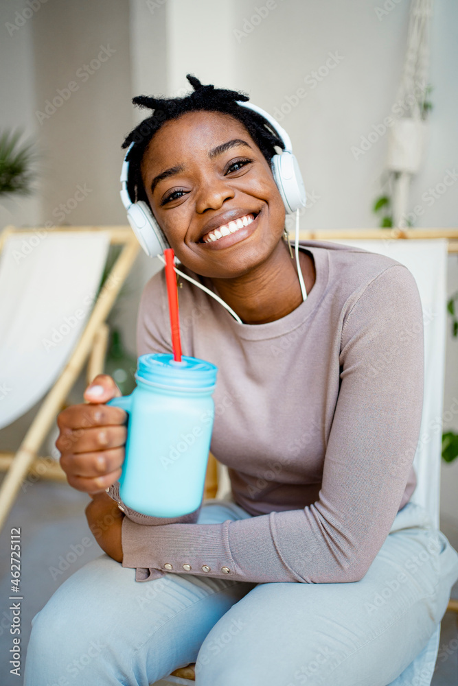 Smiling woman with mason jar sitting on deck chair in living room Smiling woman with mason jar sitting on deck chair in living room