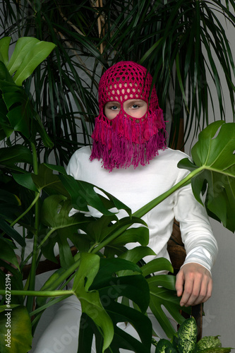 Portrait of teenage girl wearing crocheted pink headdress sitting between house plants