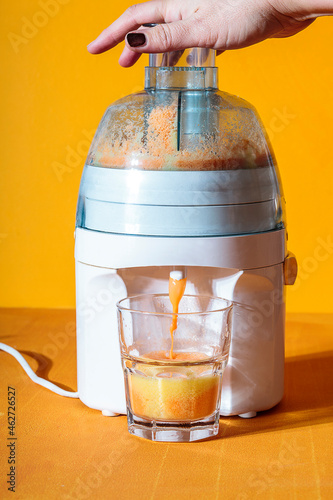 Female hand resting on top of juicer pouring carrot juice into glass