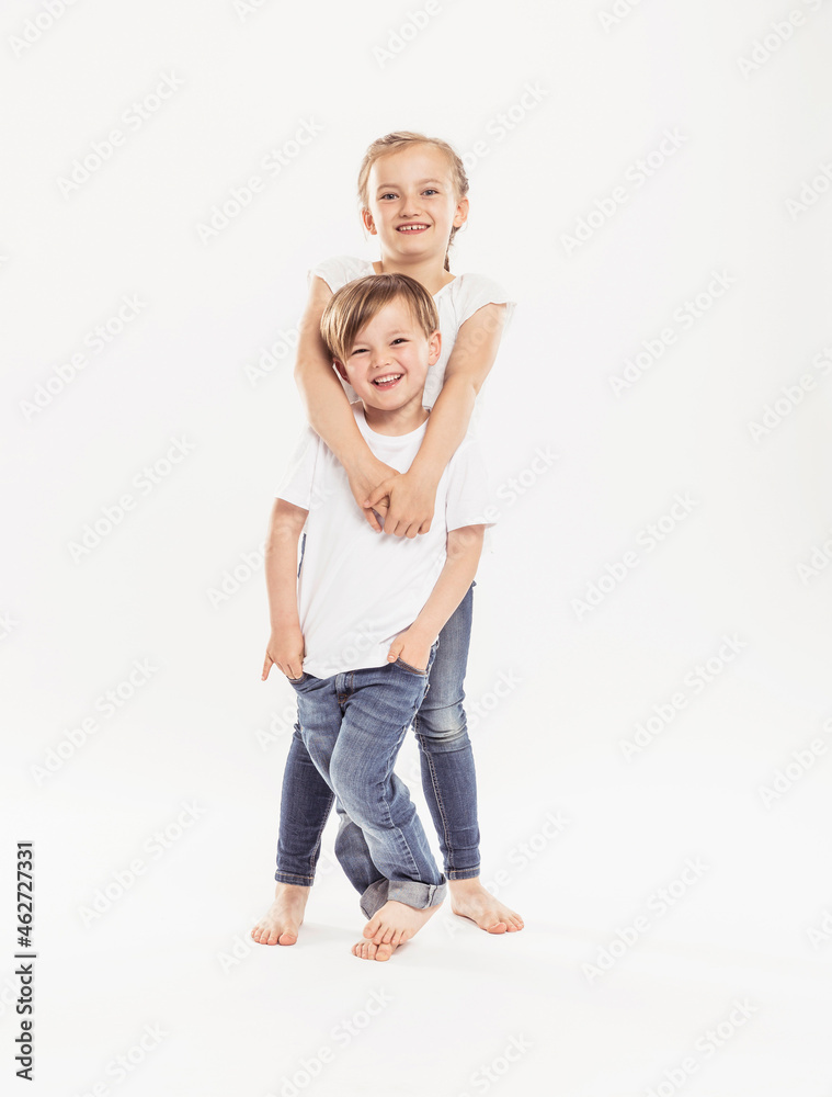 Portrait of smiling girl and her younger brother standing in front of white background Portrait of smiling girl and her younger brother standing in front of white background