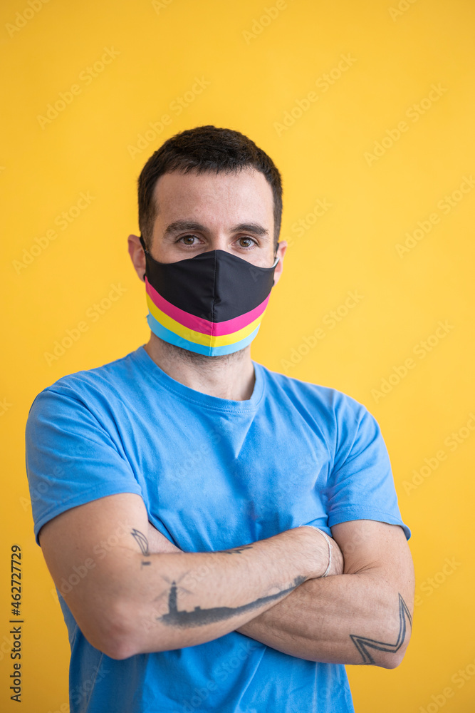 Close-up of man wearing multi colored mask with arms crossed standing against yellow background Close-up of man wearing multi colored mask with arms crossed standing against yellow background
