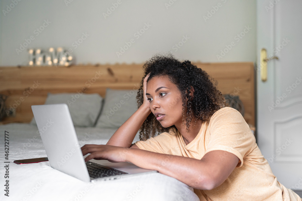 Stressed young woman with head in hand using laptop on bed at home Stressed young woman with head in hand using laptop on bed at home
